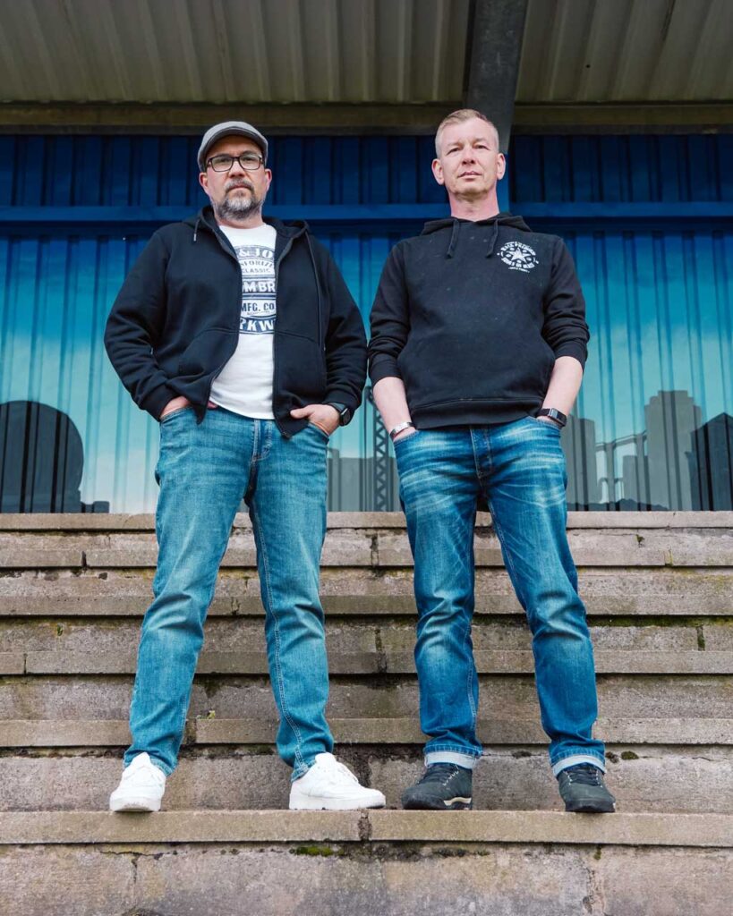 Bandfoto von den Stadtrandpoeten – einem Folk/Pop Duo aus Bochum im Ruhrgebiet. Die Musiker Oliver Wengeler und Peter Albert stehen auf der Zuschauertribüne am Rasenplatz von SV Blau-Weiß Weitmar 09 e.V.